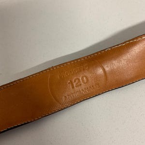 K&ouml;nnte beinhalten: Nahaufnahme eines braunen Lederg&uuml;rtels mit wei&szlig;en N&auml;hten an den Kanten. Das Innere des G&uuml;rtels zeigt den gepr&auml;gten Text: "PRODOTTO 120 ARTIGIANALE". Der G&uuml;rtel ist wahrscheinlich 120 cm lang.