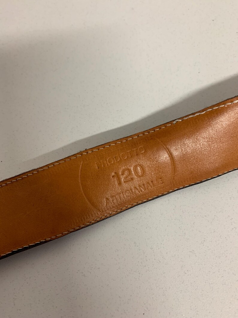 K&ouml;nnte beinhalten: Nahaufnahme eines braunen Lederg&uuml;rtels mit wei&szlig;en N&auml;hten an den Kanten. Das Innere des G&uuml;rtels zeigt den gepr&auml;gten Text: "PRODOTTO 120 ARTIGIANALE". Der G&uuml;rtel ist wahrscheinlich 120 cm lang.