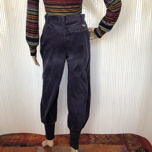 May include: Purple corduroy pants with a cuffed hem. The pants have a button fly and a back pocket.