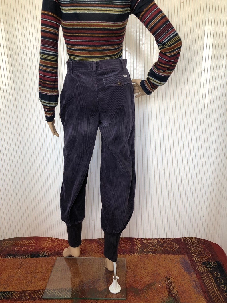 May include: Purple corduroy pants with a cuffed hem. The pants have a button fly and a back pocket.