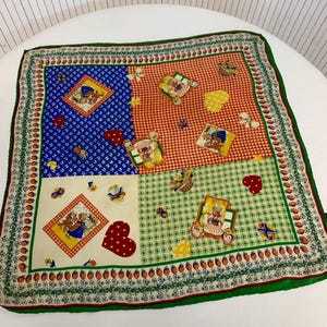 Puede incluir: Pañuelo cuadrado con diseño de patchwork. Presenta secciones azules, rojas, verdes y crema, cada una con un patrón diferente. Los patrones incluyen cuadros, flores e ilustraciones de conejos, corazones y mariposas. El pañuelo tiene un borde verde.