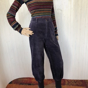 May include: Purple corduroy pants with a wide leg and cuffed bottoms. The pants have a high waist and are made of a soft, comfortable fabric.