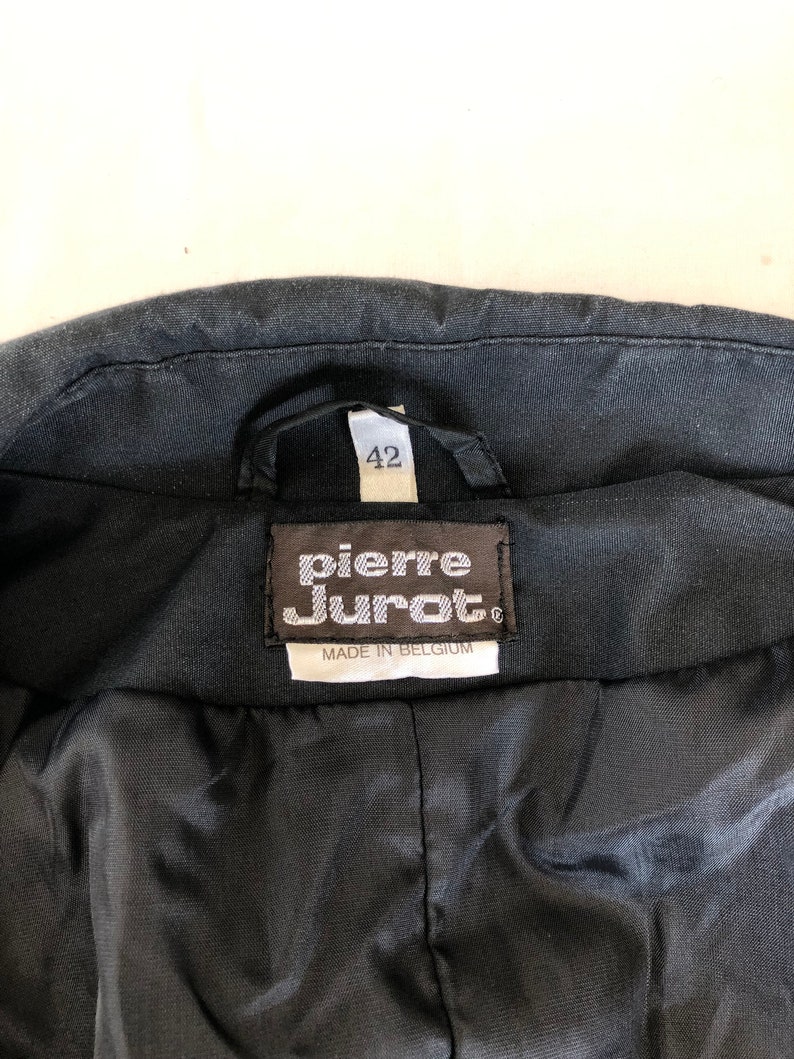 May include: Black leather jacket with a label that reads "Pierre Cardin" and "Made in Belgium". The label also has a size tag that says "42".