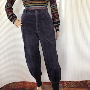 May include: Purple corduroy pants with a high waist and cuffed legs. The pants have a relaxed fit and are made of a soft, comfortable fabric.