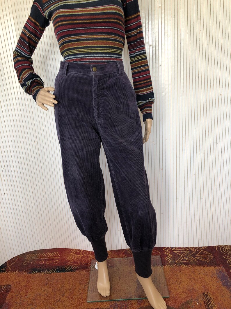 May include: Purple corduroy pants with a high waist and cuffed legs. The pants have a relaxed fit and are made of a soft, comfortable fabric.