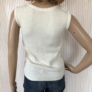 May include: A white sleeveless sweater with a ribbed texture. The sweater is made of a soft, lightweight material.