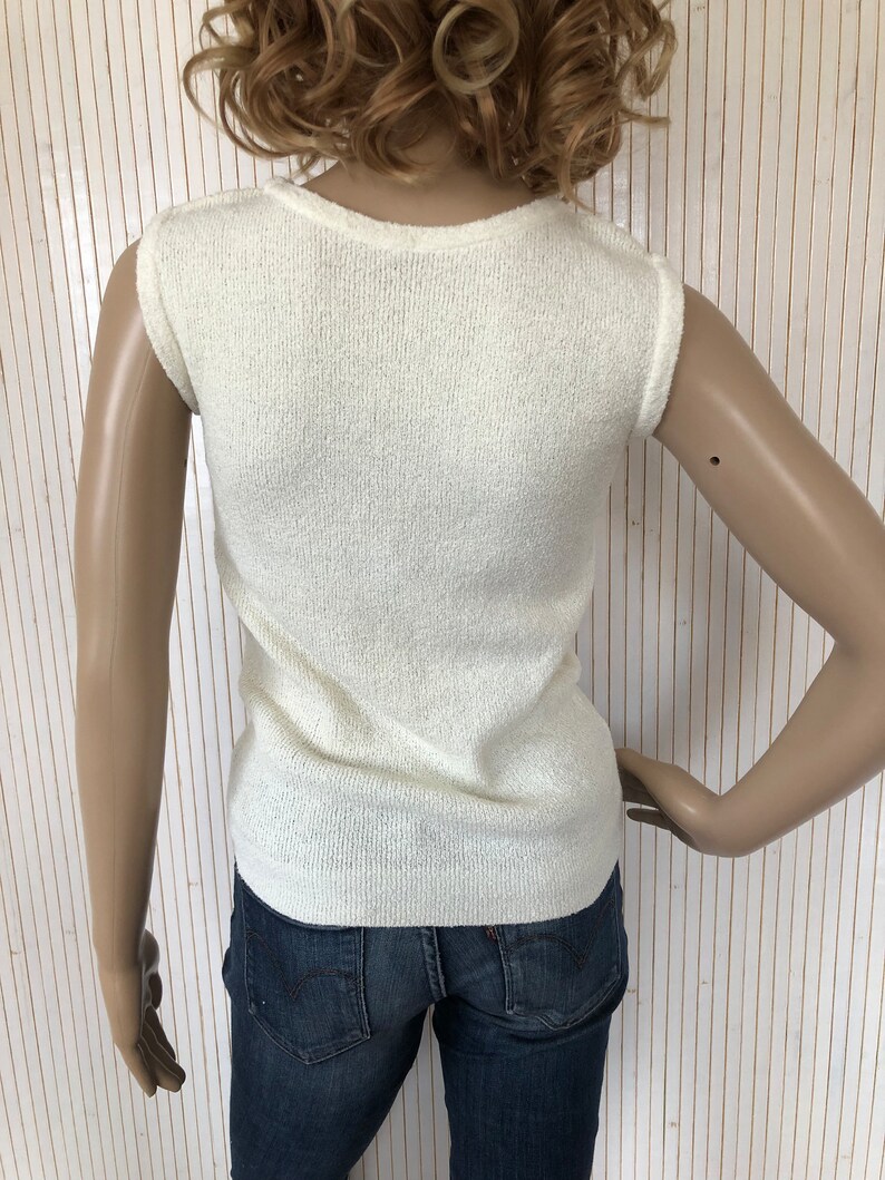 May include: A white sleeveless sweater with a ribbed texture. The sweater is made of a soft, lightweight material.