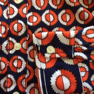 K&ouml;nnte beinhalten: Nahaufnahme eines rot-wei&szlig;-blauen gemusterten Hemdes mit wei&szlig;en Kn&ouml;pfen. Das Hemd hat ein geometrisches Design mit einem sich wiederholenden Muster aus Kreisen.
