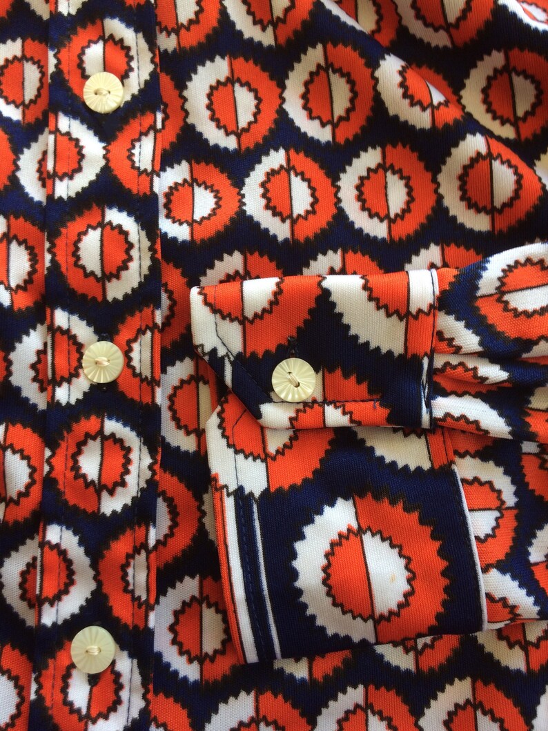 K&ouml;nnte beinhalten: Nahaufnahme eines rot-wei&szlig;-blauen gemusterten Hemdes mit wei&szlig;en Kn&ouml;pfen. Das Hemd hat ein geometrisches Design mit einem sich wiederholenden Muster aus Kreisen.