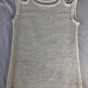 May include: A white sleeveless sweater with gold embellishments on the shoulders.