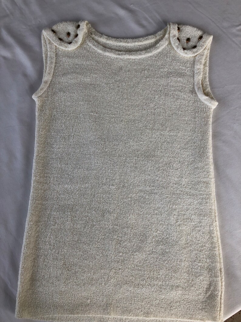 May include: A white sleeveless sweater with gold embellishments on the shoulders.