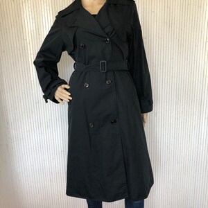 May include: A black double-breasted trench coat with a belt. The coat has a classic design and is made of a smooth fabric.