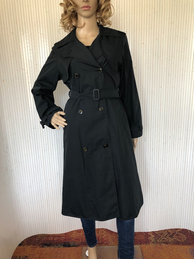 May include: A black double-breasted trench coat with a belt. The coat has a classic design and is made of a smooth fabric.