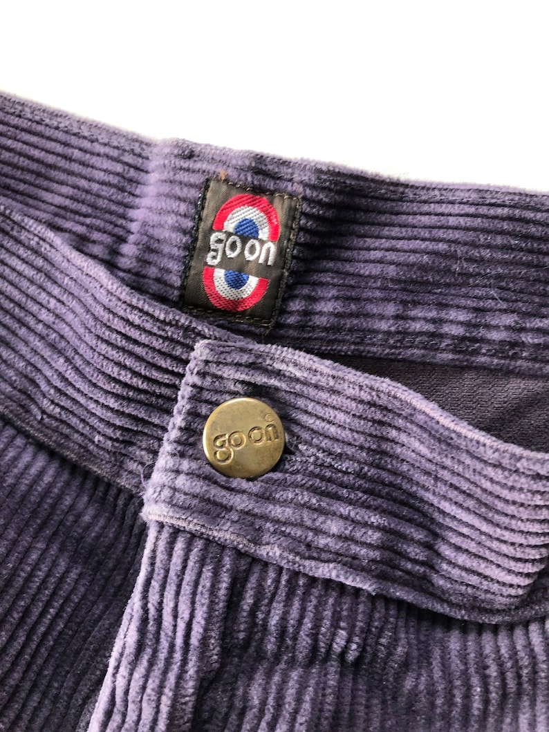 May include: Purple corduroy pants with a gold button and a label that says "goon" in a circle with red, white, and blue accents.