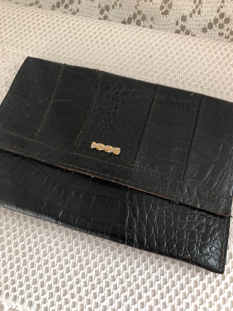 May include: A black leather wallet with a crocodile-embossed pattern and a gold-toned clasp.