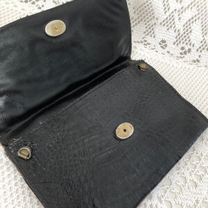 May include: Black leather clutch purse with a textured crocodile pattern and two gold-toned snap closures.