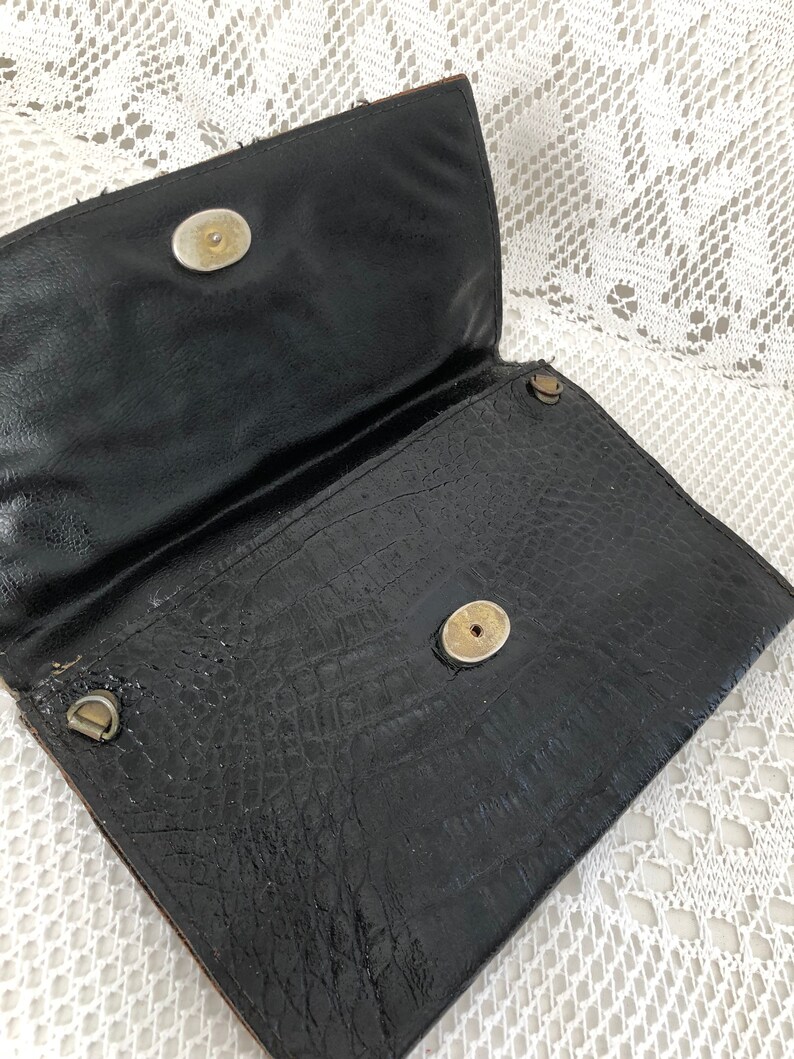 May include: Black leather clutch purse with a textured crocodile pattern and two gold-toned snap closures.