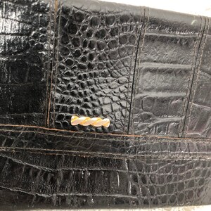 May include: Black leather clutch with a crocodile embossed pattern and a gold-toned clasp.