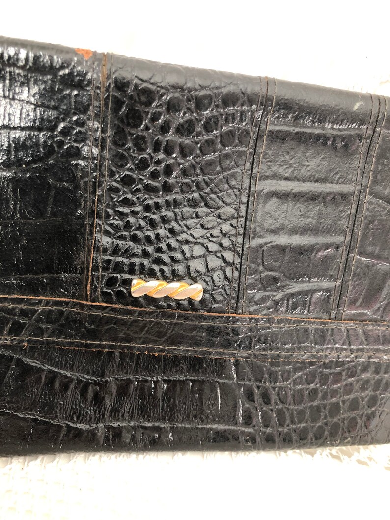 May include: Black leather clutch with a crocodile embossed pattern and a gold-toned clasp.