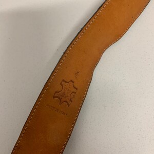 K&ouml;nnte beinhalten: Nahaufnahme eines braunen Lederg&uuml;rtels mit hellbraunem Innenraum. Der G&uuml;rtel hat wei&szlig;e N&auml;hte an den Kanten und die Worte "MADE IN ITALY" sind sichtbar. Ein Lederstempel ist ebenfalls sichtbar.