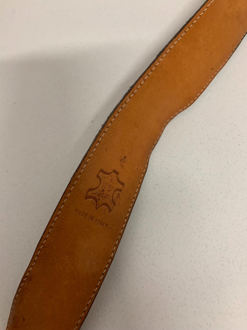 K&ouml;nnte beinhalten: Nahaufnahme eines braunen Lederg&uuml;rtels mit hellbraunem Innenraum. Der G&uuml;rtel hat wei&szlig;e N&auml;hte an den Kanten und die Worte "MADE IN ITALY" sind sichtbar. Ein Lederstempel ist ebenfalls sichtbar.