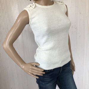 May include: A white sleeveless knit top with a round neckline and decorative accents on the shoulders.