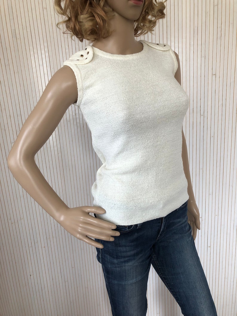 May include: A white sleeveless knit top with a round neckline and decorative accents on the shoulders.