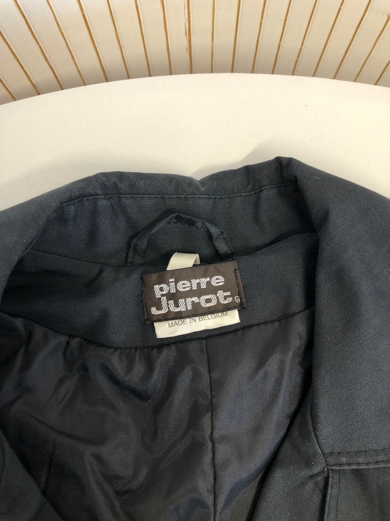 May include: A black jacket with a label that reads "Pierre Jurat" and "Made in Belgium".