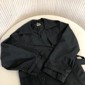 May include: A black double-breasted trench coat with a belt. The coat has a label that reads "Pierre Cardin" on the inside collar.