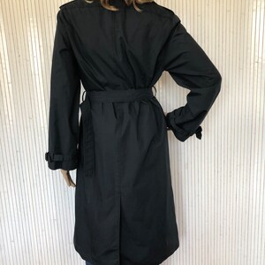 May include: A black long-sleeved trench coat with a belt. The coat has a classic design and is made of a durable fabric.