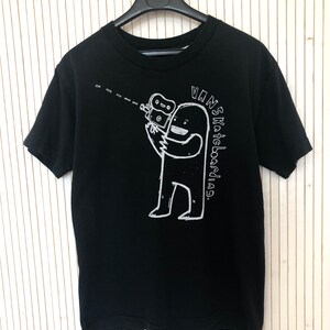 May include: Black t-shirt with a white graphic of a cartoon monster holding a camera. The text "VANS Skateboard" is written vertically on the right side of the graphic.