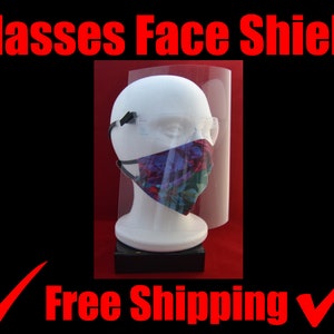 May include: A clear plastic face shield with a black elastic band. The face shield is worn over a floral patterned face mask. The text "Glasses Face Shield" is written in red letters at the top of the image. The text "Free Shipping" is written in red letters at the bottom of the image.
