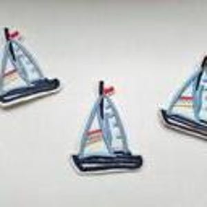 May include: Three white fabric sailboat patches with blue and red details. The sailboats are outlined in black and have a white background.