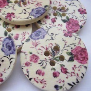 May include: A set of round, white buttons with a floral pattern in shades of pink, purple, and green. The buttons have three holes each.