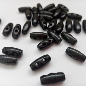 May include: A group of black wooden toggle buttons with two holes each. The buttons are scattered on a white surface.