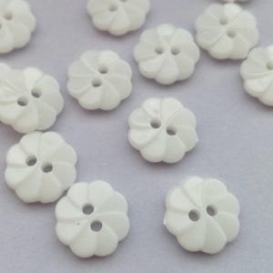 以下が含まれることがあります： 渦巻き模様の白いプラスチックボタンのコレクション。ボタンは2つの穴があり、直径は約2.5cmです。