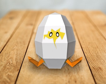 May include: A white papercraft egg with yellow eyes and beak, partially hatched, with orange papercraft legs. The egg is sitting on a wooden surface.