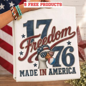 Può includere: T-shirt bianco con un design patriottico. Il testo recita "1776 Freedom Made in America". La grafica include un'oca con occhiali da sole e un cappello con il design della bandiera americana e una bolla di gomma da masticare con i colori della bandiera francese.