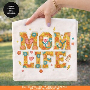 May include: A white t-shirt with the words "MOM LIFE" in a colorful, retro design. The design includes flowers, hearts, baby feet, a stethoscope, and a baby bottle. The text "9 FREE AMAZING PNGS INCLUDED" is in a black circle.