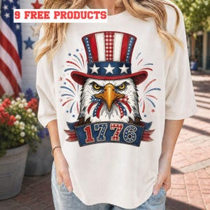 May include: Cream-colored t-shirt featuring a patriotic design. The graphic includes an eagle wearing a red, white, and blue Uncle Sam hat, with the year "1776" on a banner. Fireworks and stars complete the design.