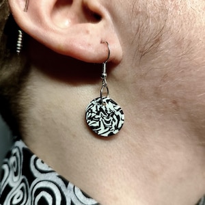 Può includere: Un paio di orecchini pendenti in argento con un design astratto bianco e nero sul ciondolo circolare.