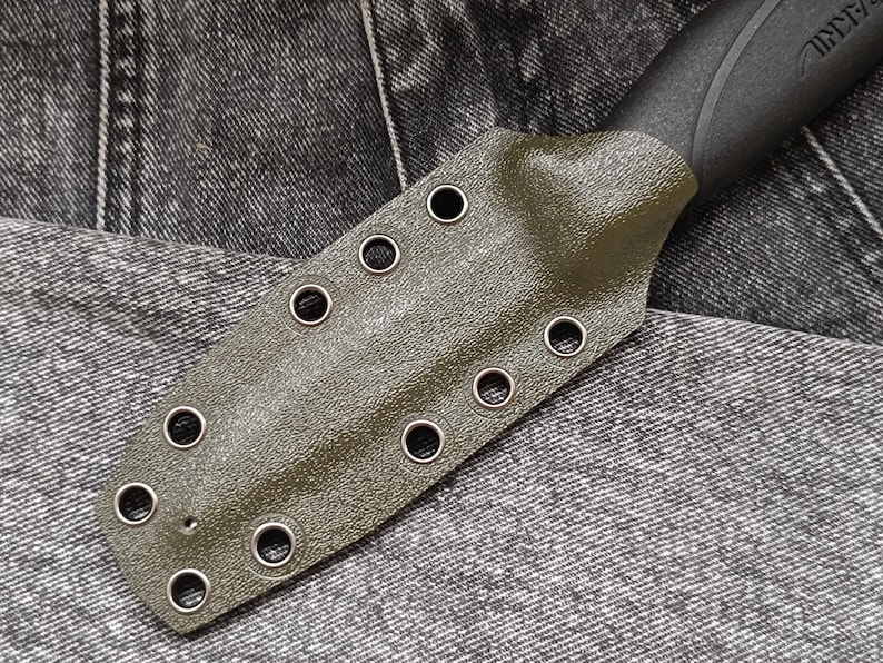 May include: A green leather knife sheath with metal eyelets. The sheath has a textured surface and is designed to fit a knife with a black handle.
