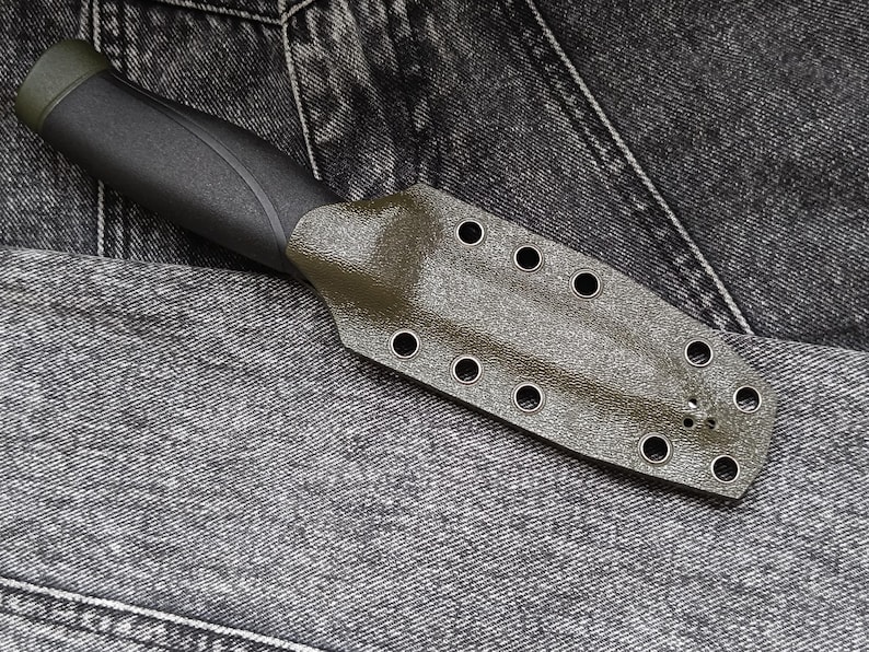 May include: A dark green knife sheath with multiple eyelets. The sheath is made of a textured material and has a black handle.
