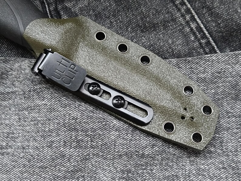 May include: A green leather knife sheath with a black metal clip. The clip has the text "ULTRACLIP" on it. The sheath has multiple holes around the edge.