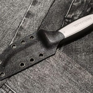 Op de afbeelding: Een Morakniv-mes met een grijs handvat en een zwarte, getextureerde schede. De schede is voorzien van zes metalen oogjes aan de zijkant voor bevestiging. Het handvat van het mes is gedeeltelijk zichtbaar met de merknaam Morakniv in reliëf.