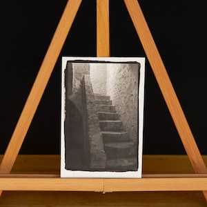 May include: Black and white photograph of a stone staircase leading up to a doorway in a building. The photo is mounted on a wooden easel.