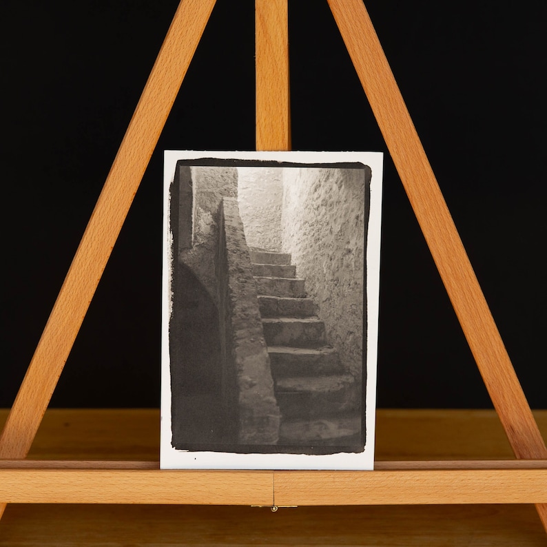 May include: Black and white photograph of a stone staircase leading up to a doorway in a building. The photo is mounted on a wooden easel.