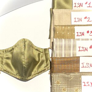 May include: Six fabric swatches in various shades of brown and beige with a white background. Each swatch has a handwritten label with the text "ISN" followed by a number from 1 to 6. A green face mask with a checkered pattern is in the foreground.