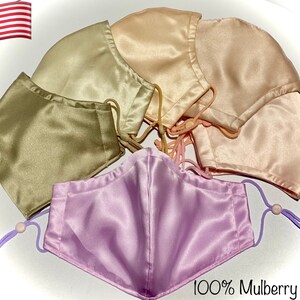 May include: Five face masks made of 100% mulberry silk in various shades of beige, pink, and lavender. The masks are arranged in a semi-circle with the text "100% Mulberry Silk" at the bottom.