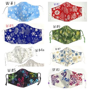 May include: Ten different fabric face masks with snowflake patterns. The masks are in various colors, including blue, red, green, white, black, and silver. The masks are all made of cotton fabric and have elastic ear loops.